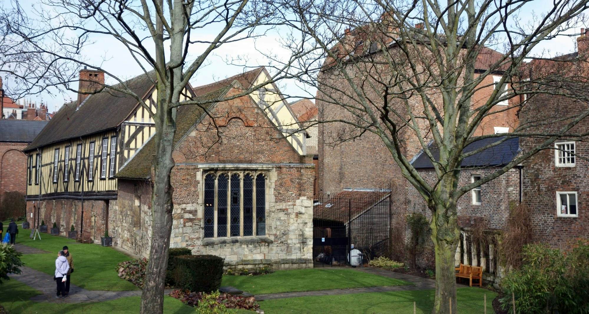 York, UK - February 19, 2013: Merchant Adventurers Hall was constructed in the fourteenth century and is still in use today. An senior couple is strolling in the grounds and tow men in the background are picking up litter.